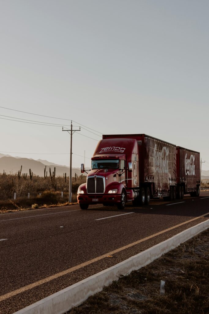 A large red truck transports goods along a desert highway under a clear sky.