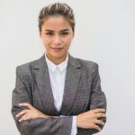 Portrait of a confident Asian woman in a plaid blazer with arms crossed, smiling and posing.